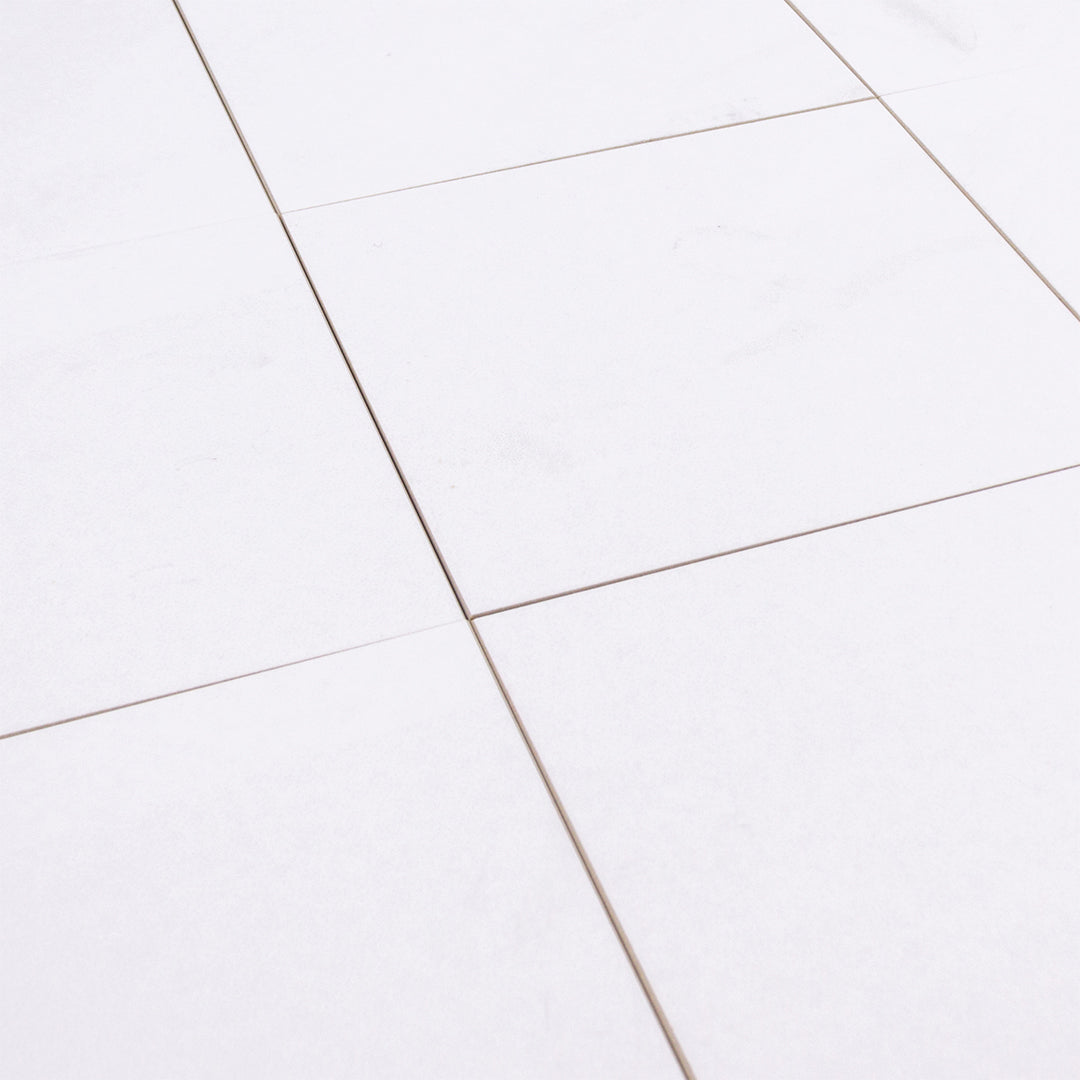 Angled close up of several 5x5 white stone look tiles that have a matte finish and a subtle pattern.