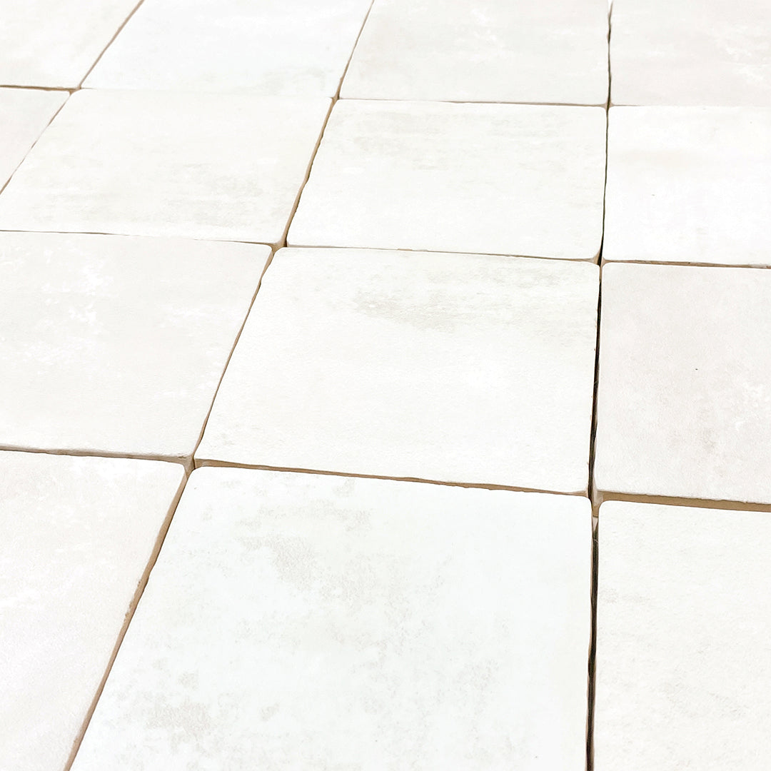 Angled close up of a group of 4x4 satin zellige tiles named white. they have a handmade look, textured edges and a subtle colour variation