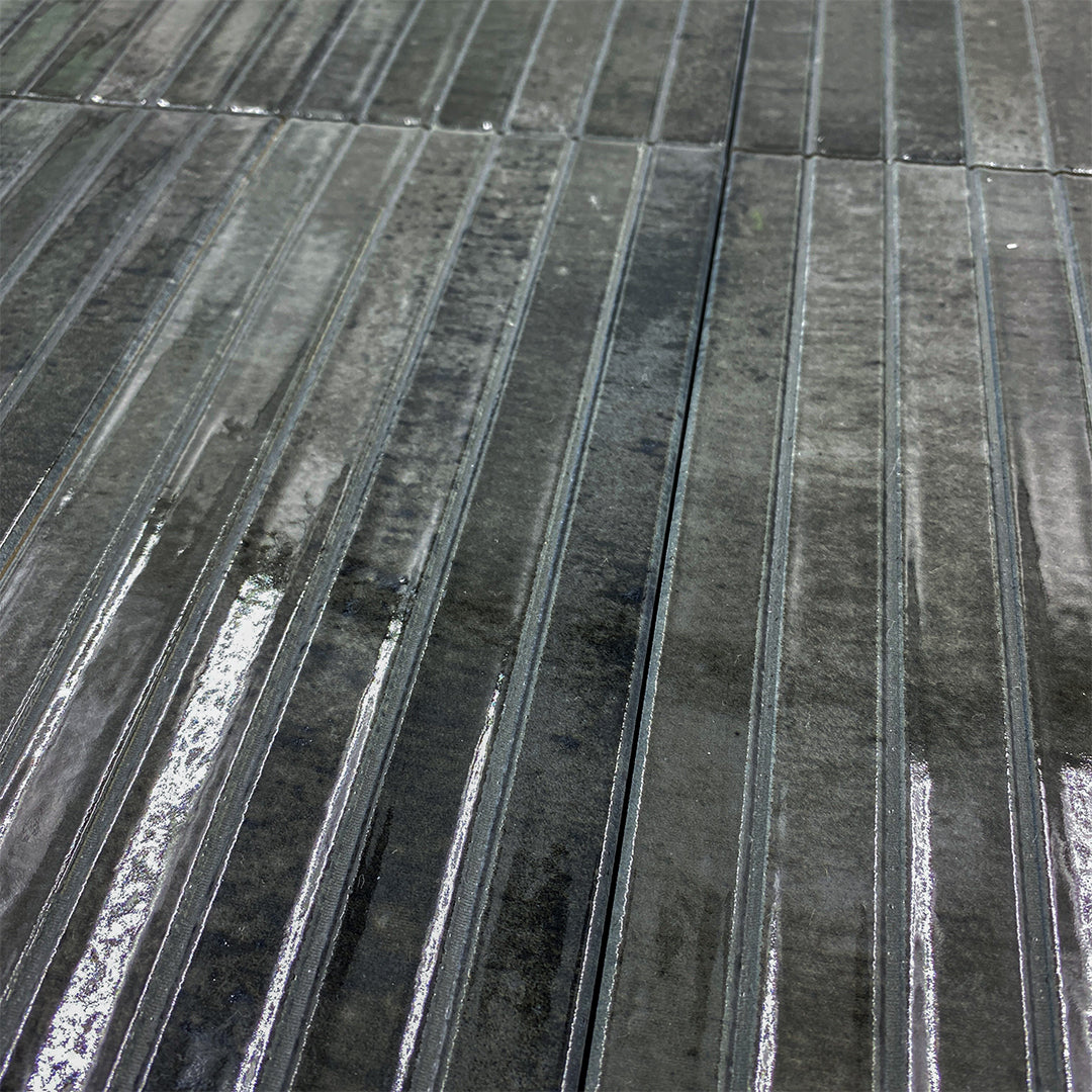 Angled close up of a group of 5x10 panel tiles in glossy black, the tile has a 3D linear faux grout line kitkat look. 