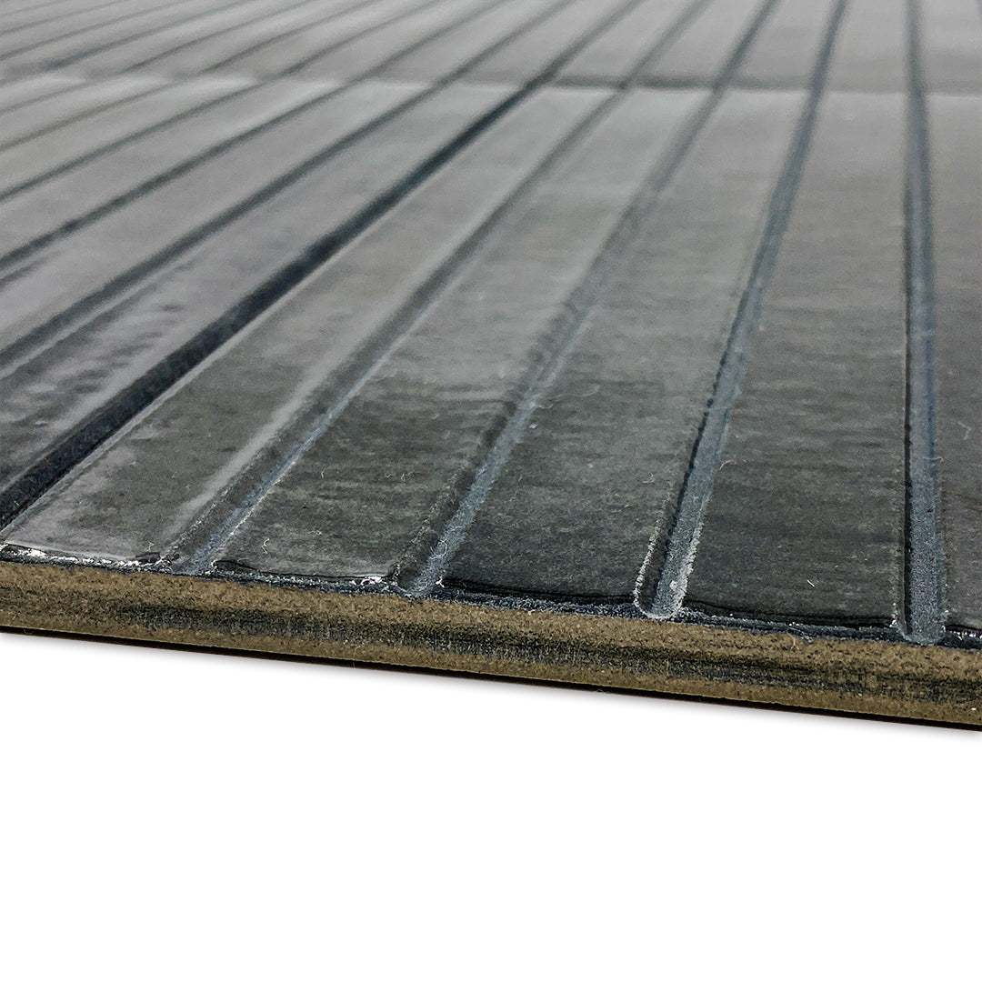 Angled close up of a single 5x10 panel tile in glossy black, the tile has a 3D linear faux grout line kitkat look. This angles highlights the depth and texture of the grooves. 