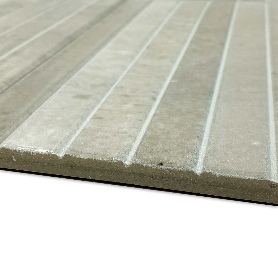 Angled close up of the edge of a single 5x10 panel tile in glossy grey, the tile has a 3D linear faux grout line kitkat look and colour variation. This angle shows the depth and texture of the lines. 