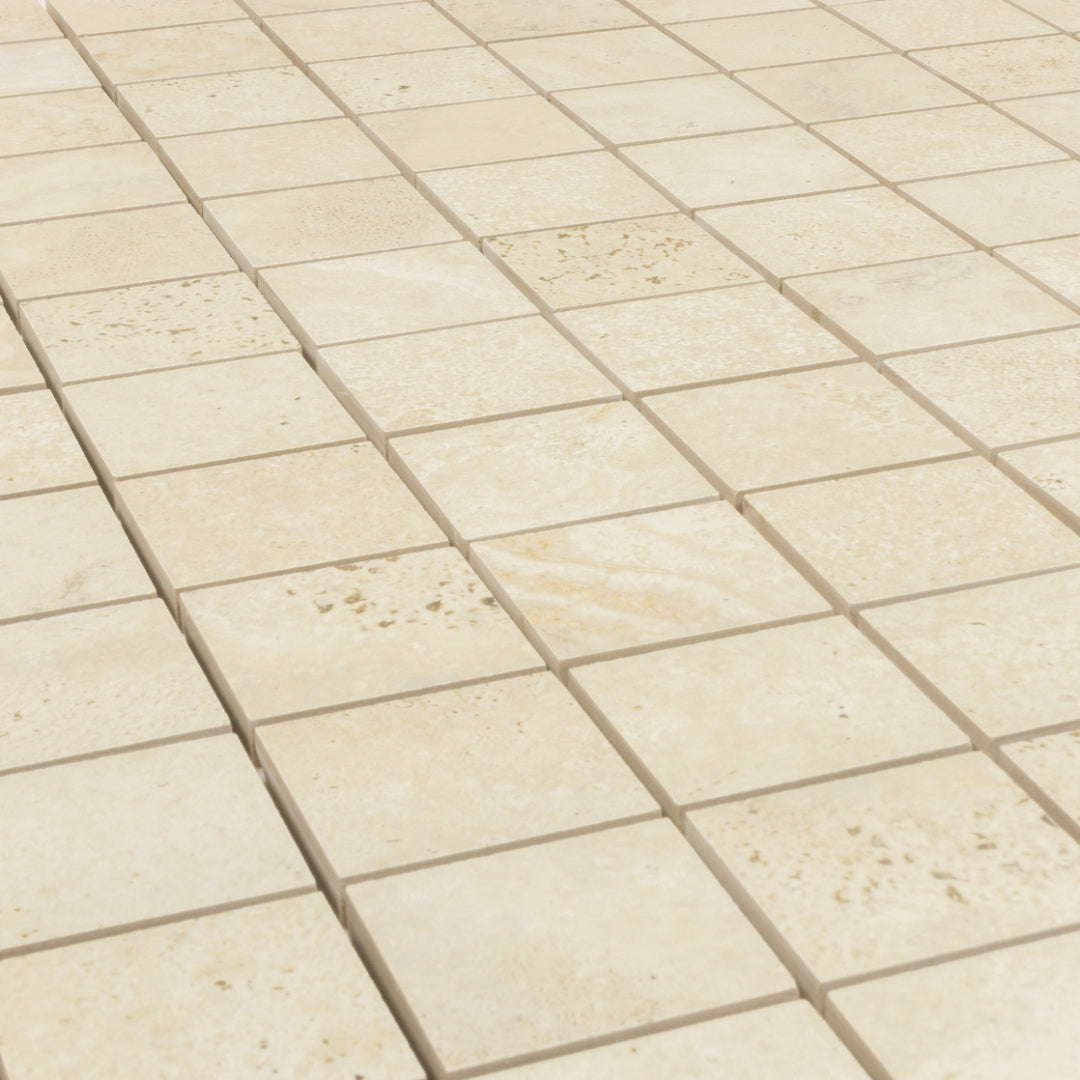 Angled close up of a 2x2 square mosaic tile that resembles travertine stone in beige. 