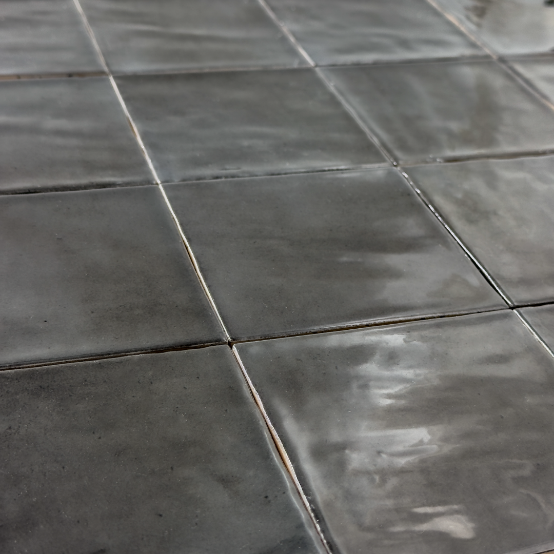 Angled close up view of a group of nine glossy 4x4 black tiles. Highlighting the slight colour variations, texture and finish.