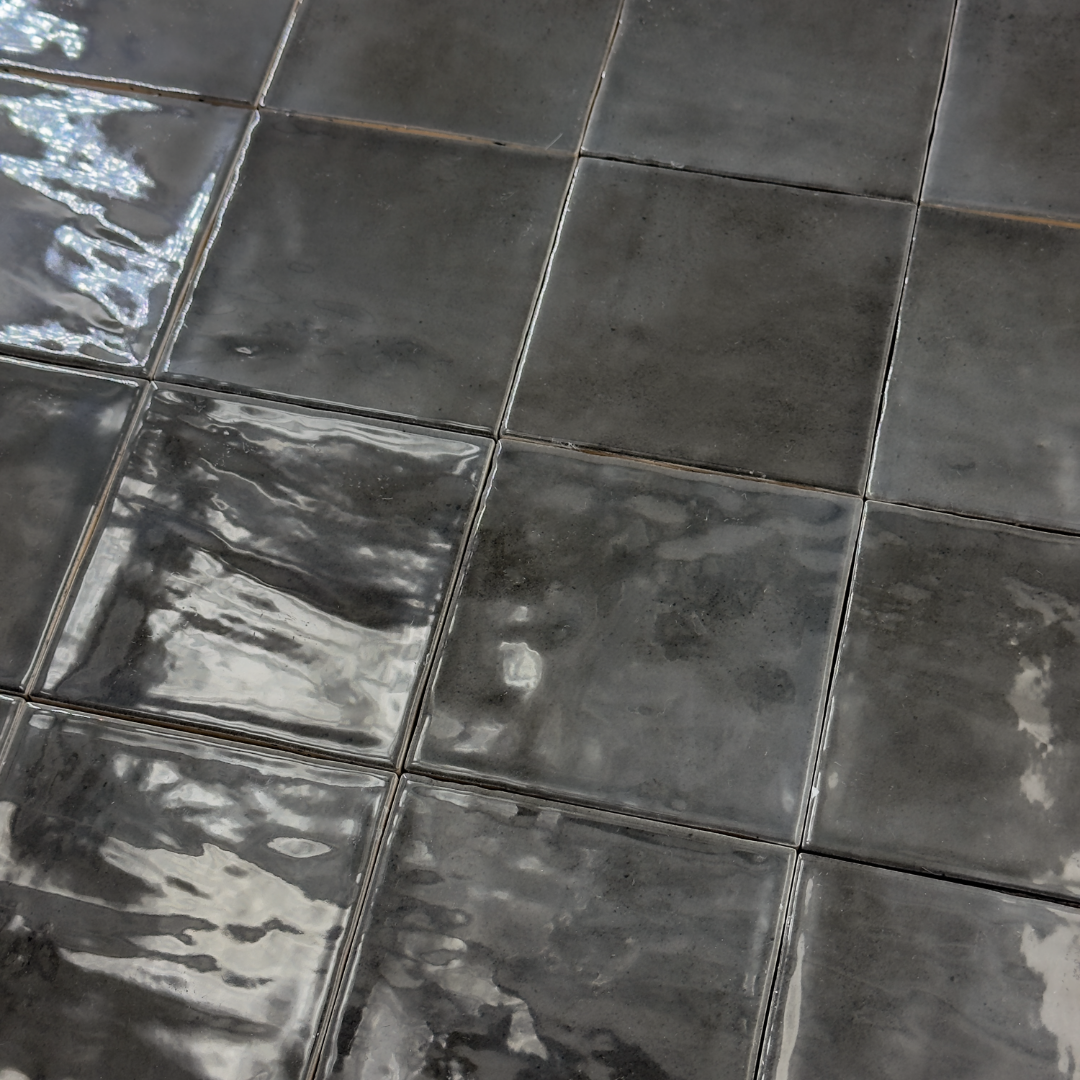 Angled ariel view of a group of glossy 4x4 black tiles. Highlighting the slight colour variations, texture and finish.