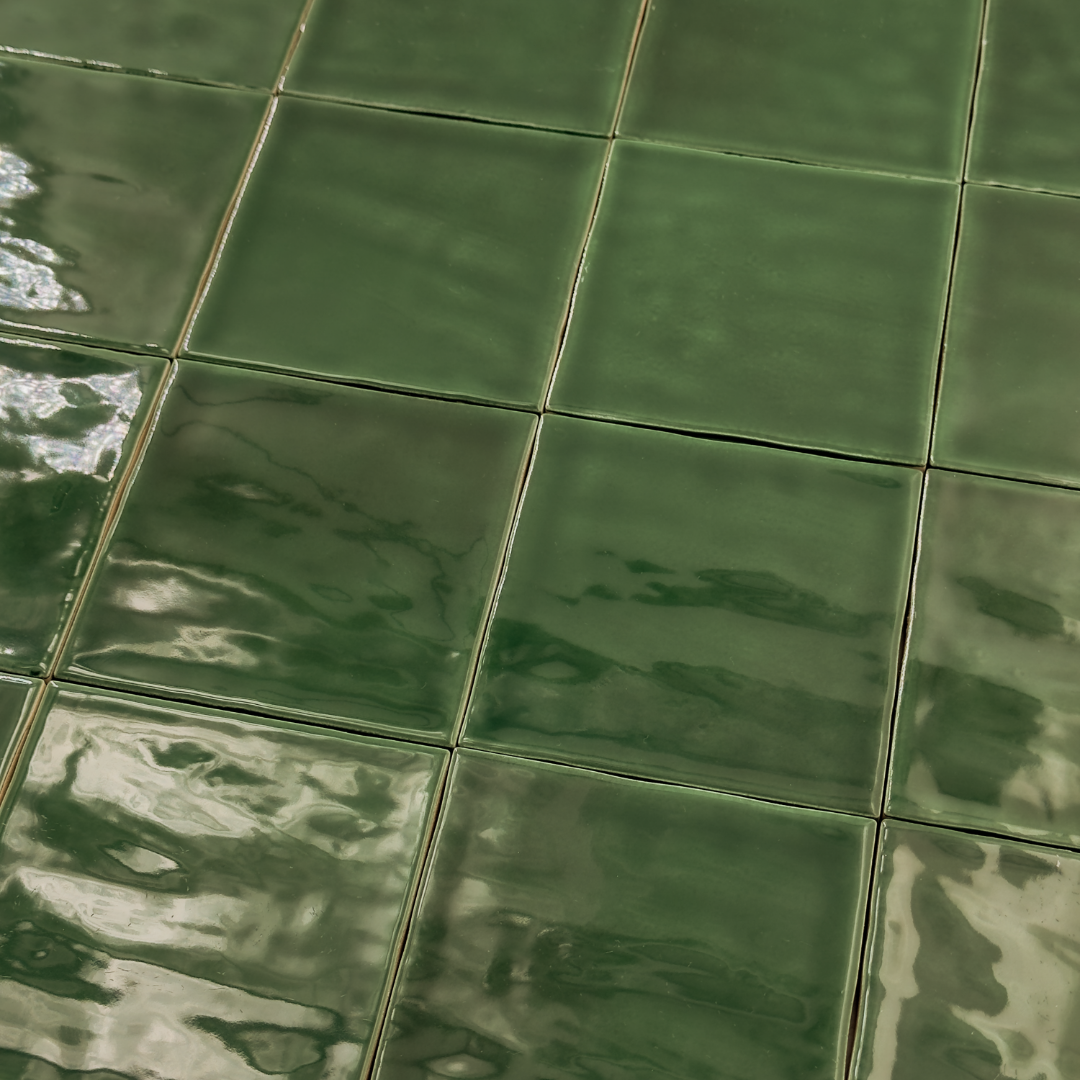 Angled ariel view of a group of glossy 4x4 textured green tiles showing the colour and texture. The glossy finish catches the light. 