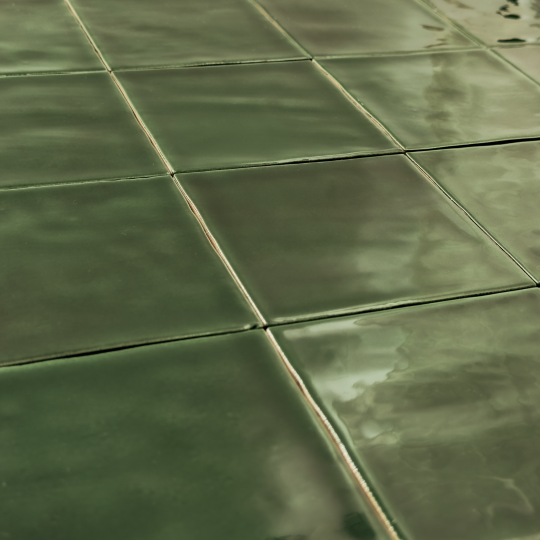 Angled close up view of a group of glossy 4x4 textured green tiles showing the colour and texture. The glossy finish catches the light. 