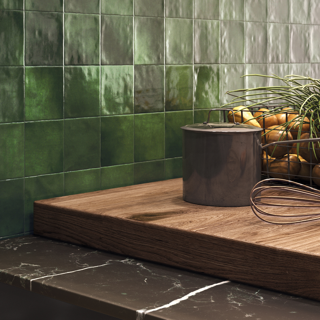 A close up of a kitchen backsplash with black counters, wood cutting board and modern vibe. The tiles are 4x4 glossy olive mossy green tiles with colour variance, and texture. 