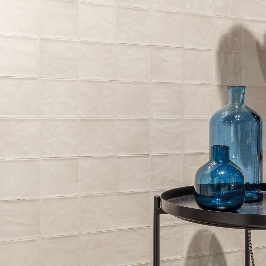 A close up of a tiled wall and modern black and blue accessories. The tile on the wall is 4x4 glossy ivory tiles that have textured edges, a slight colour variance and a shiny finish that catches the light. 