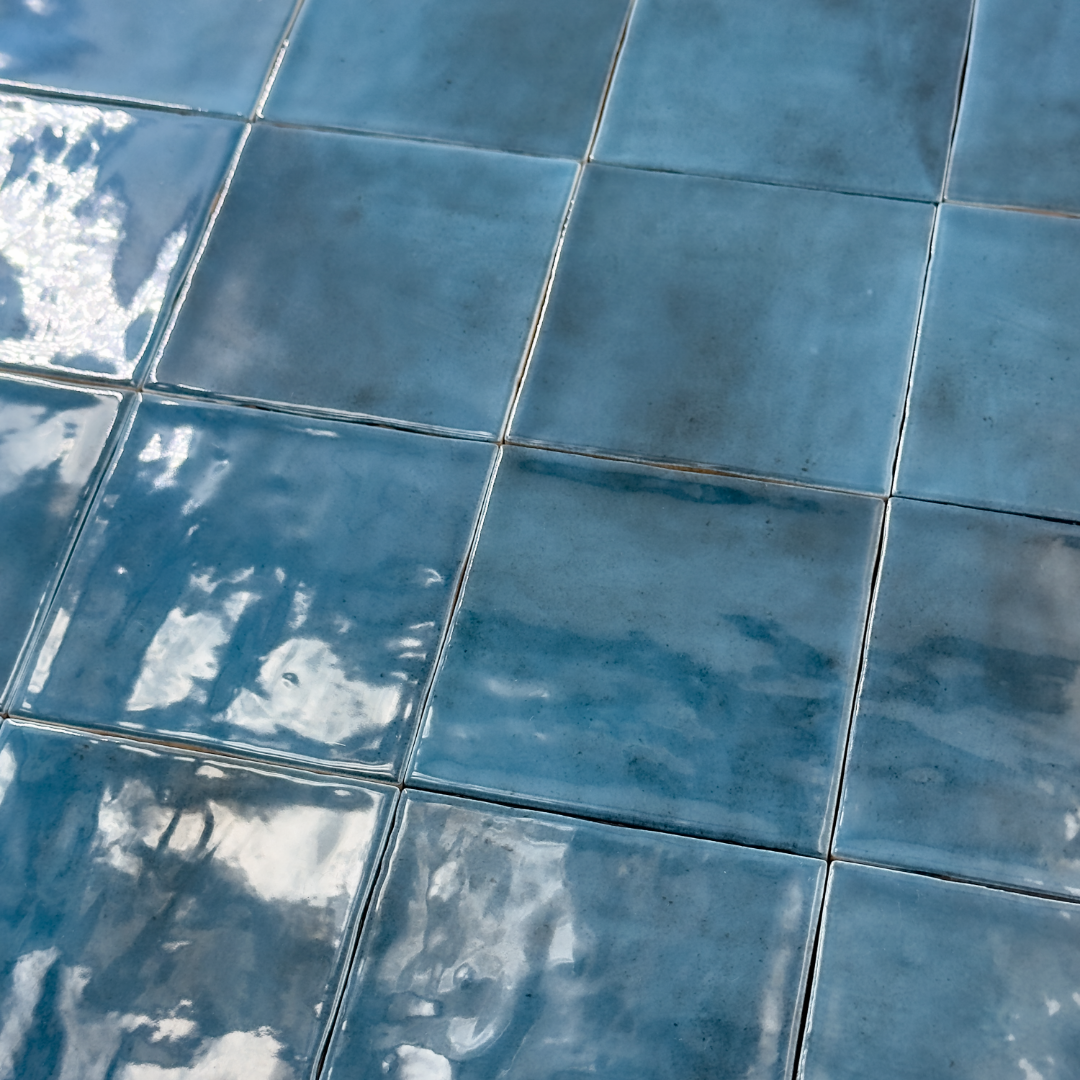 Angled ariel view of a group of glossy 4x4 textured sapphire blue tiles showing the colour and texture. The glossy finish catches the light. 