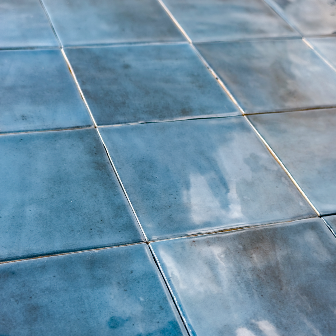 Angled close up view of a group of glossy 4x4 textured sapphire blue tiles showing the colour and texture. The glossy finish catches the light. 
