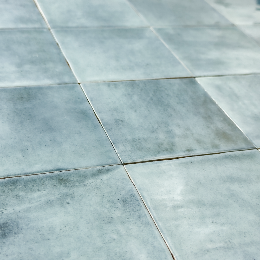Angled close up view of glossy 4x4 textured light denim blue tiles showing the colour and textured edges. 