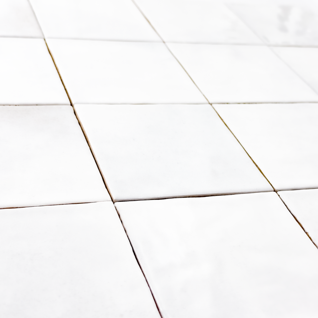 Angled close up view of a group of glossy 4x4 textured white tiles showing the textured edges. The glossy finish catches the light. 