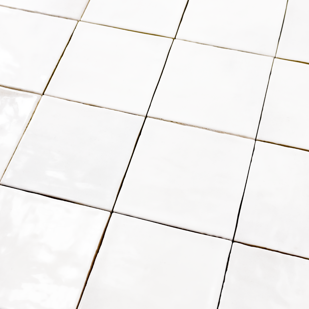Angled ariel view of a group of glossy 4x4 textured white tiles showing the textured edges. The glossy finish catches the light. 