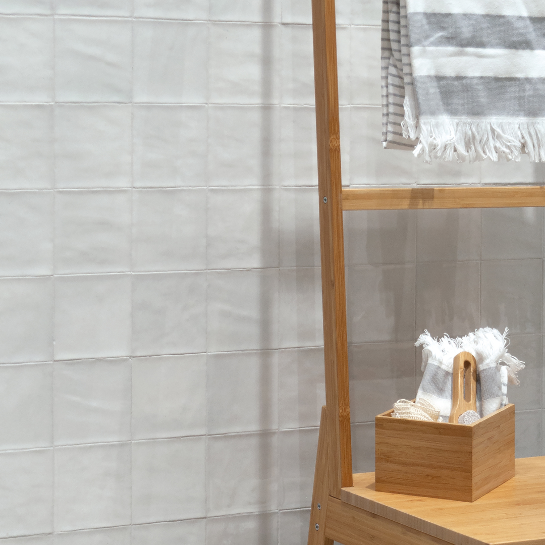 Close up view of a bathroom wall with a towel wooden leaning towel rack and wood bathroom accessories. The tiled wall is white 4x4 tiles with texture and a glossy finish. 