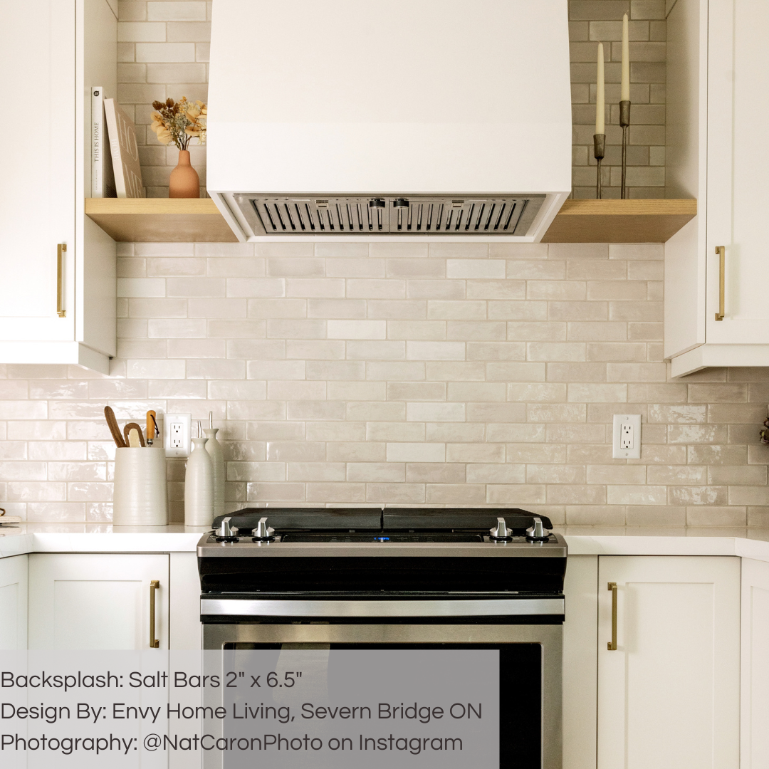 A modern white kitchen with brass accents and a tile backsplash. the tiles are 2x6.5 glossy salt subway tiles in a warm grey light beige griege with heavy colour variation. 