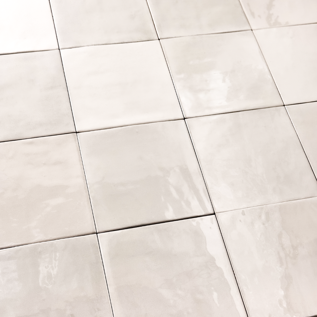 Angled ariel view of a group of glossy 5x5 textured light beige zellige tiles showing the textured edges and colour variation. 