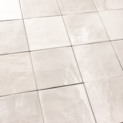 Angled ariel view of a group of glossy 5x5 textured light beige zellige tiles showing the textured edges and colour variation. 
