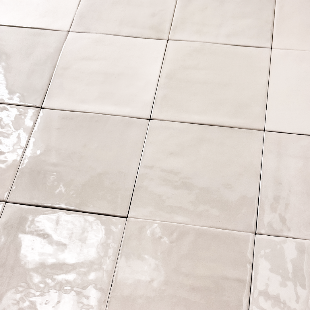Angled ariel view of a group of glossy 5x5 textured light beige zellige tiles showing the textured edges and warm colour variation. 