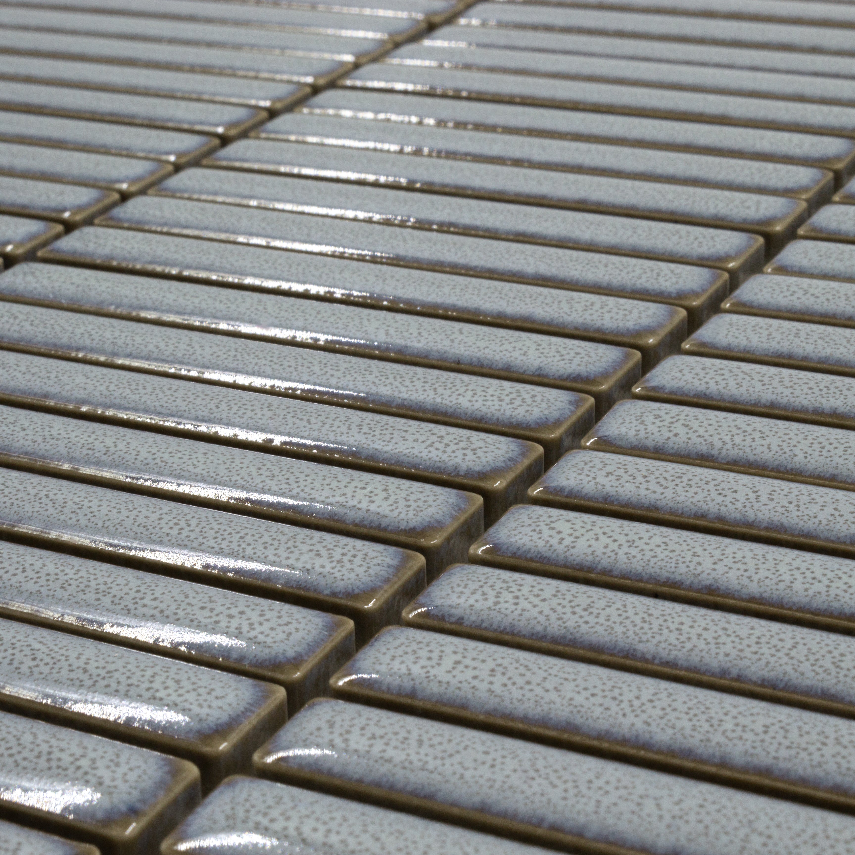 Angled close up view of a single sheet of mini kitkat stacked mosaic tiles in blue glossy. This angle features the soft coastal blue hand painted look and glossy finish. The sizing is 3/8' x 3-5/8" per tile, 10.5" X 12" per sheet
