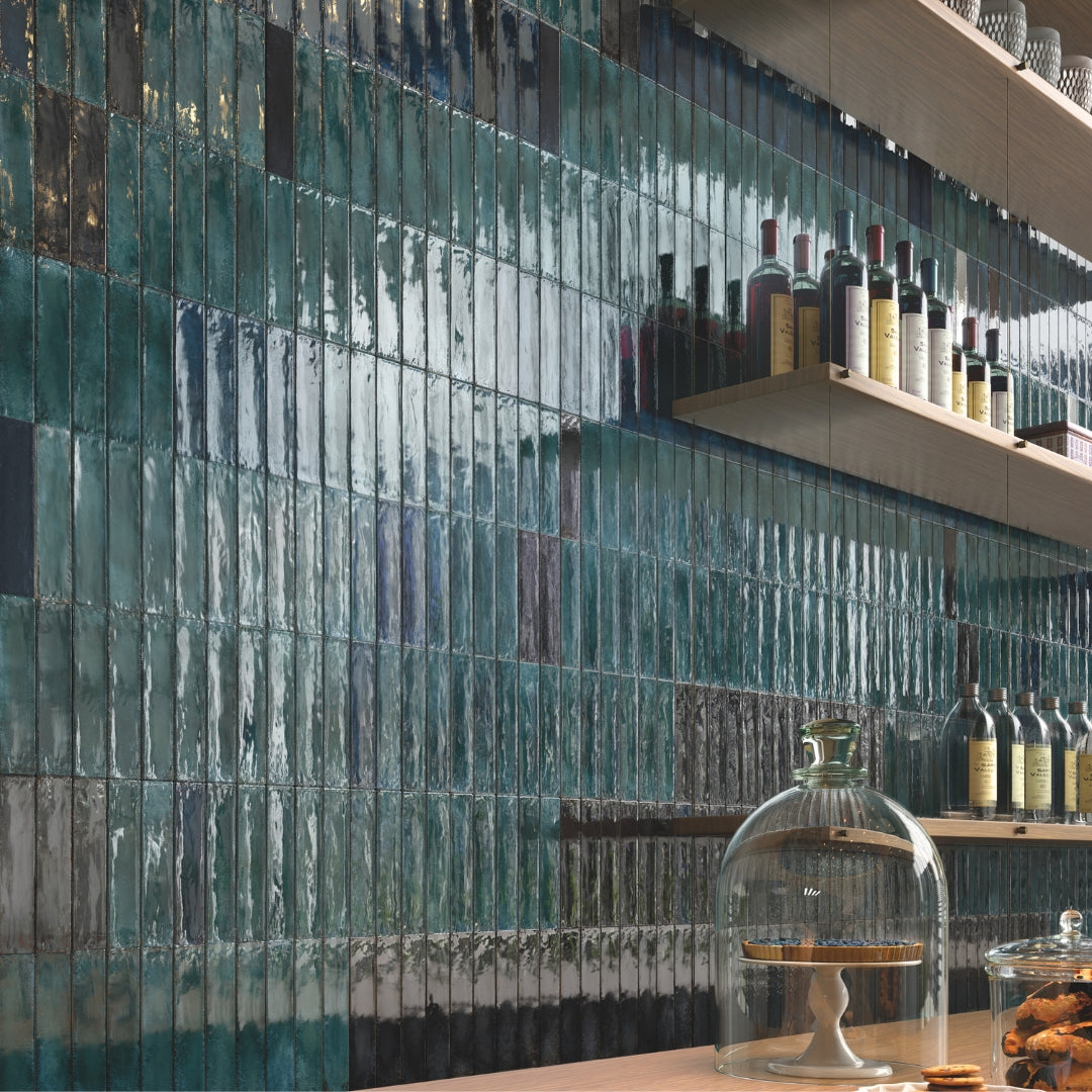 A stunning bar or kitchen backsplash with wood shelves. The backsplash tile is a glossy green 2x9 tile laid out in a vertical stack pattern. There is dimension due to the colour variation and light catching the subtle texture. 
