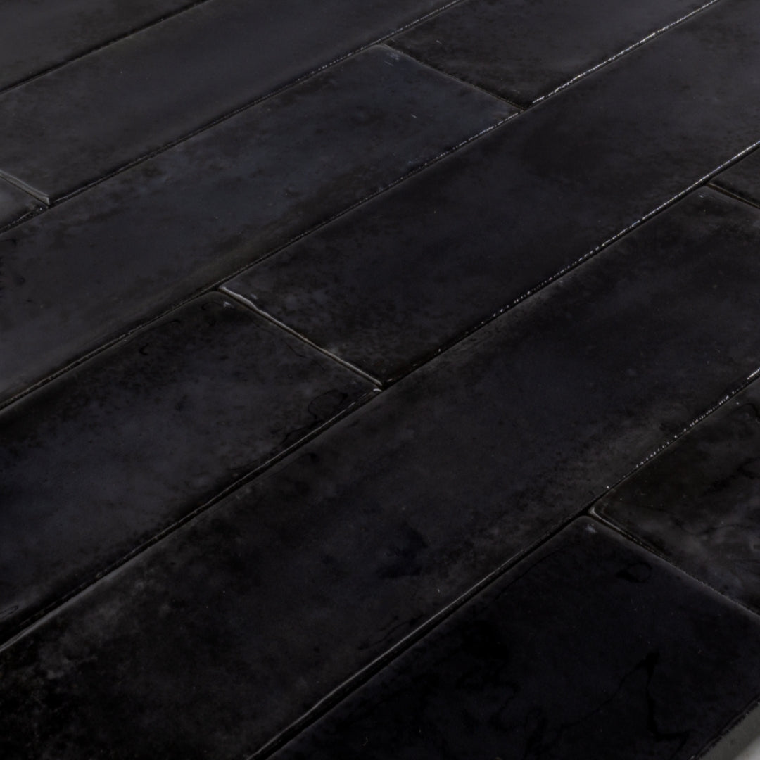 Angled close up of 2x9 black glossy tiles in a brick layout