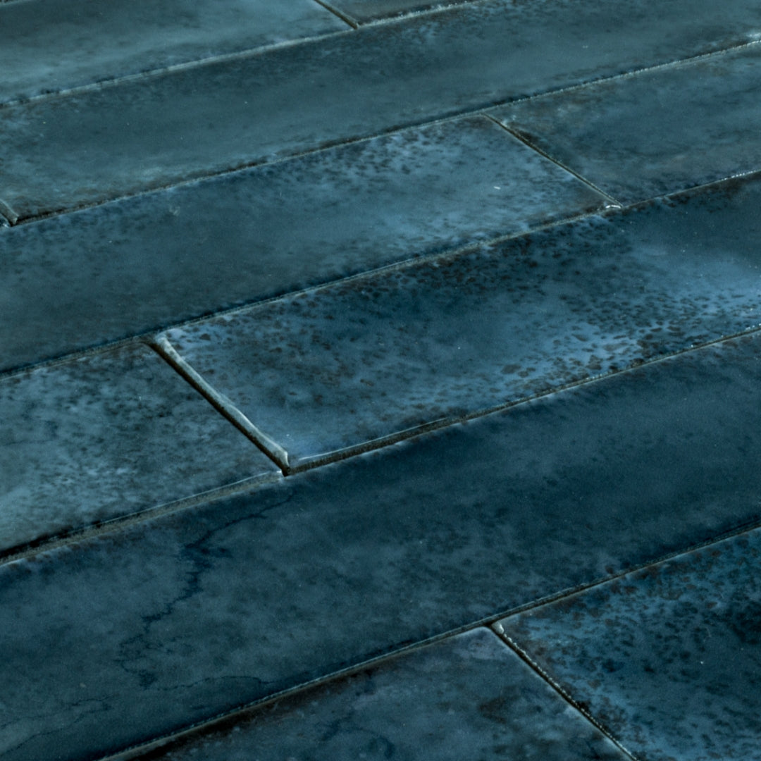 Angled close up of 2x9 blue glossy tiles in a brick layout with colour variation