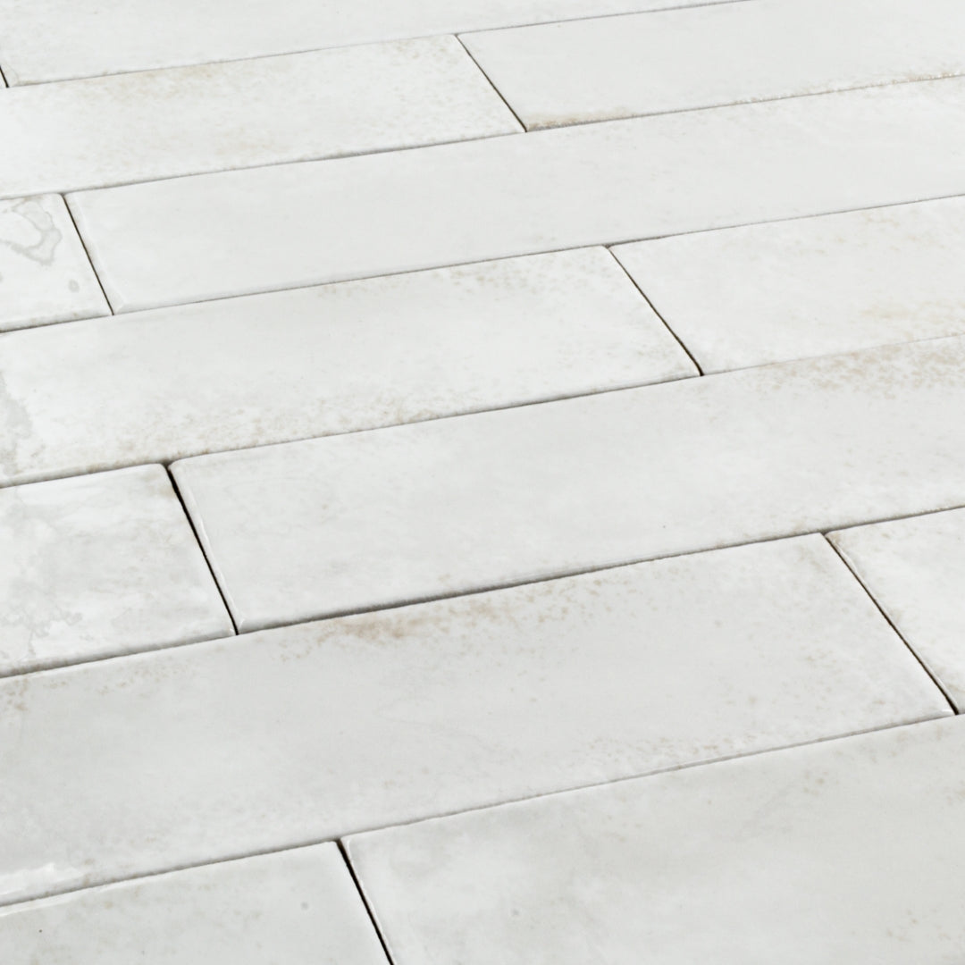 Angled close up of 2x9 white glossy tiles in a brick layout with colour variation