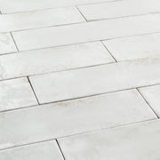 Angled close up of 2x9 white glossy tiles in a brick layout with colour variation