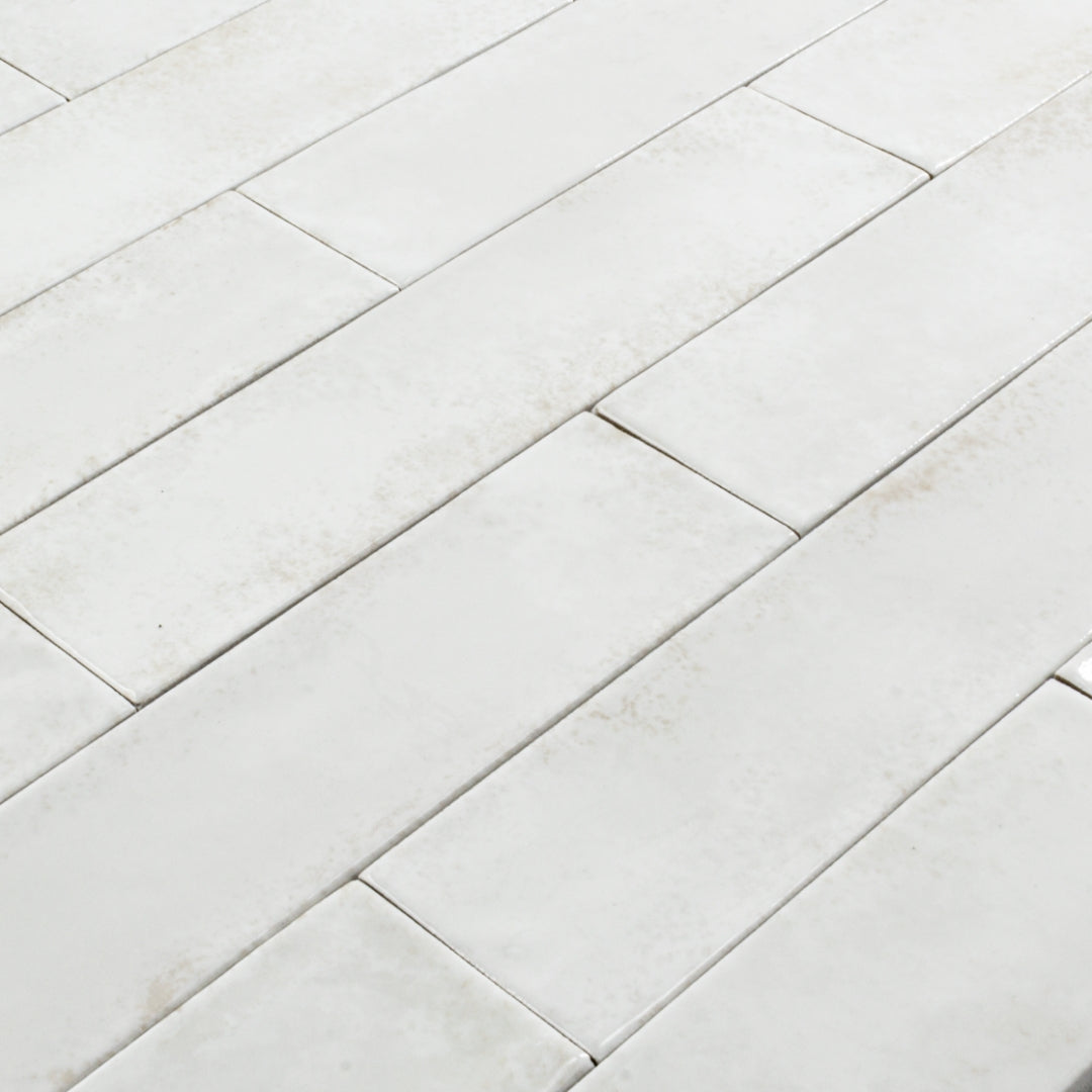 Angled close up of 2x9 white glossy tiles in a brick layout with colour variation