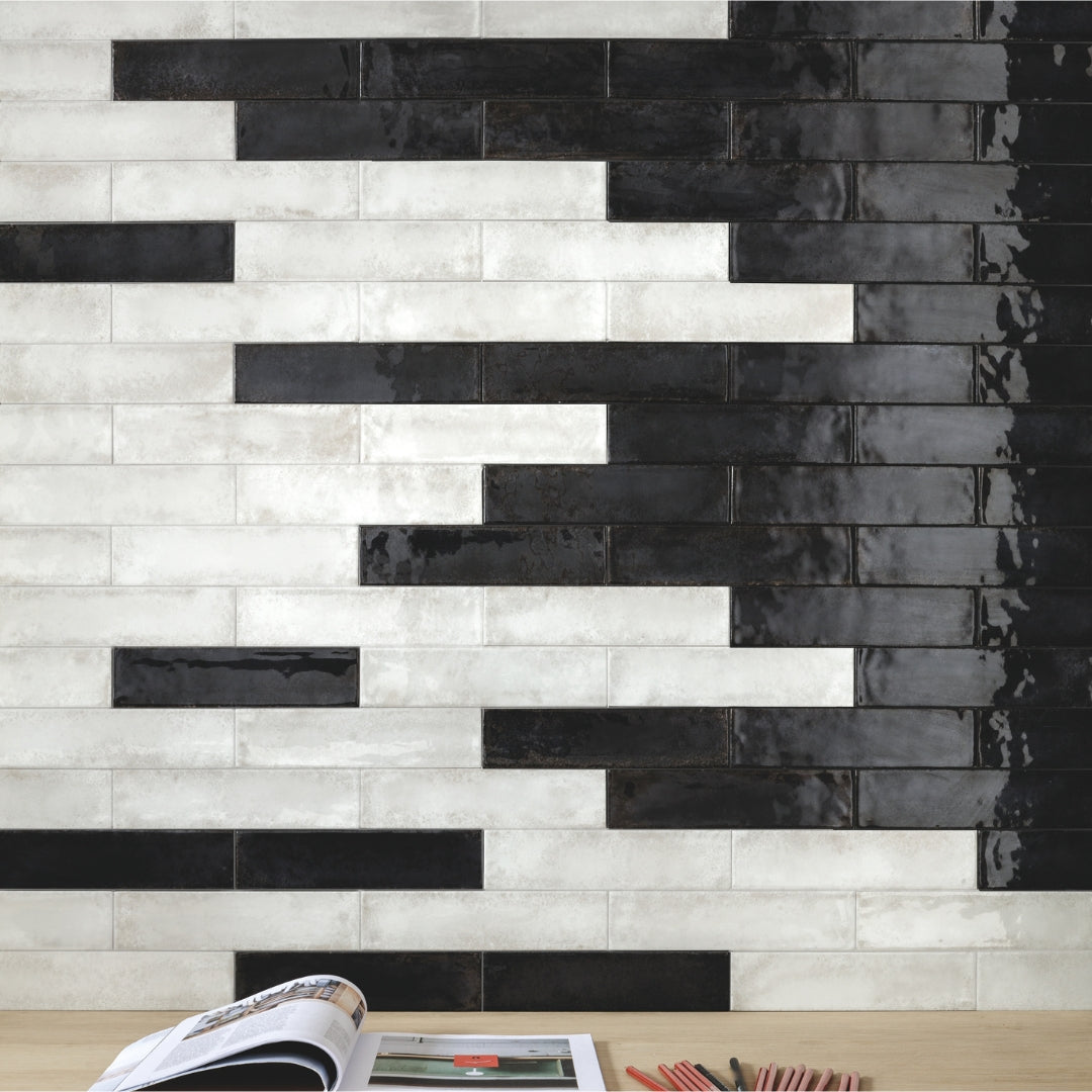 A feature wall above a desk using black and white 2x9 glossy tiles. They are mixed together in a brick layout. 