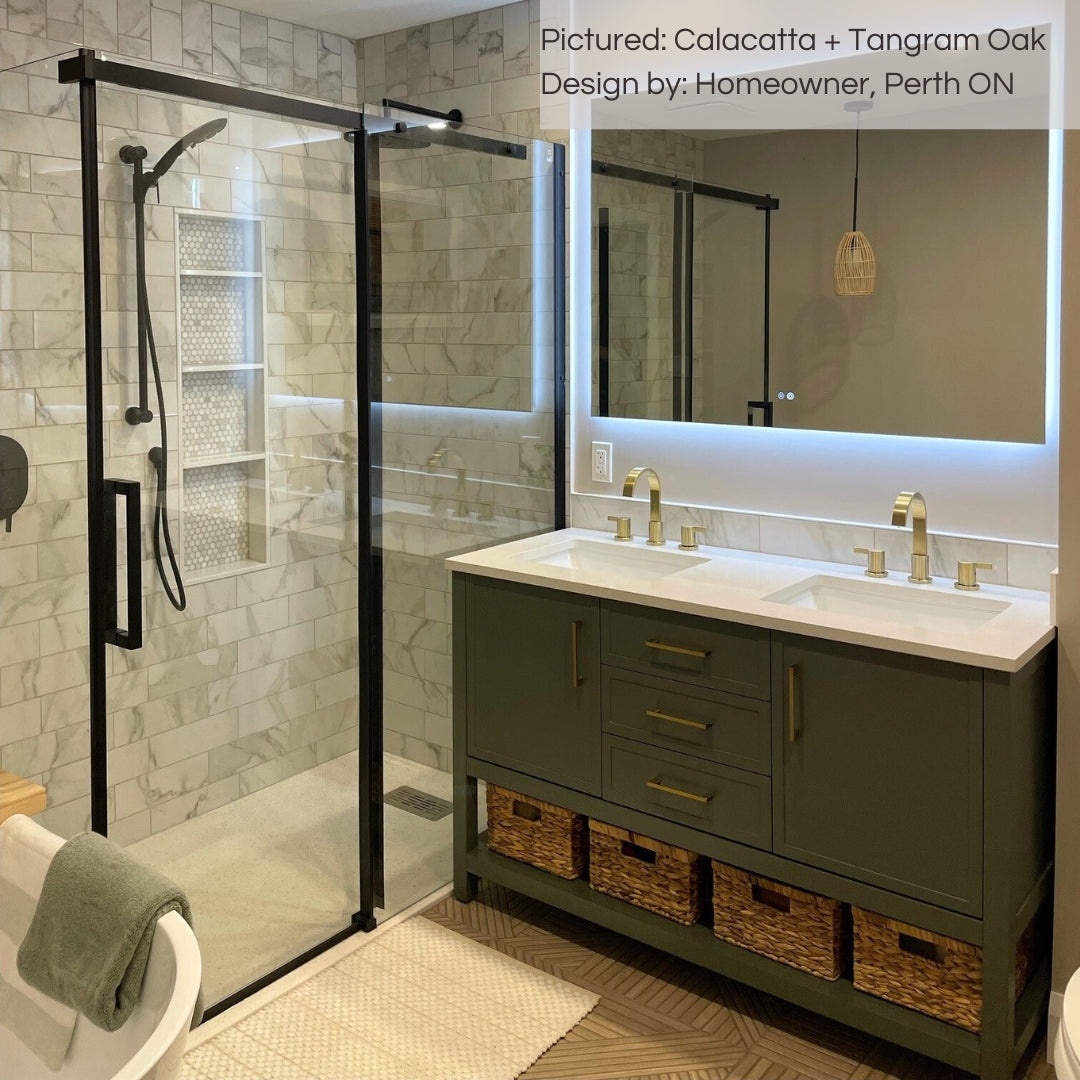 A modern bathroom with Calacatta 4x12 subway tiles on the shower walls and tangroam oak wood look geometric tiles on the floor.  the warm tones in the faux marble compliments the tangram oak. there is a olive green double vanity with gold accents. 