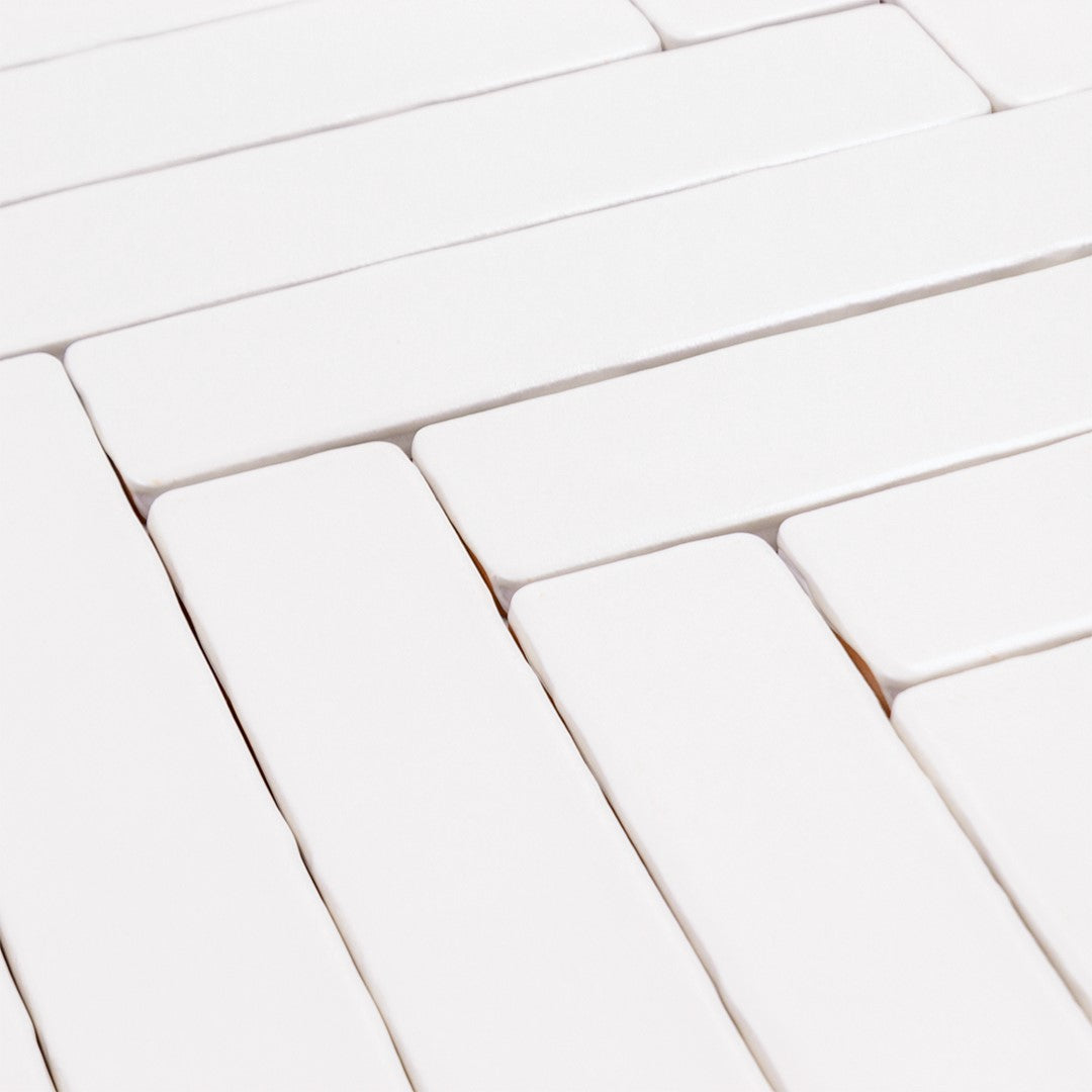 Angled close up of 2x10 candlestick matte bright white tiles lined up in a herringbone pattern so highlight the handmade edge and matte finish. 
