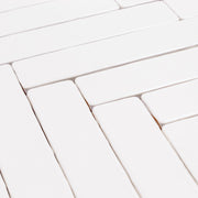 Angled close up of 2x10 candlestick matte bright white tiles lined up in a herringbone pattern so highlight the handmade edge and matte finish. 