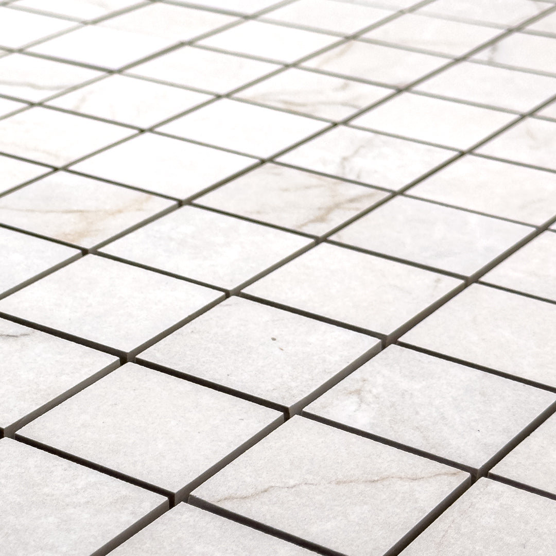 Angled close up view of a 2x2 square sheet mosaic tile that is a white bianco matte marble look with thin grey veining. 
