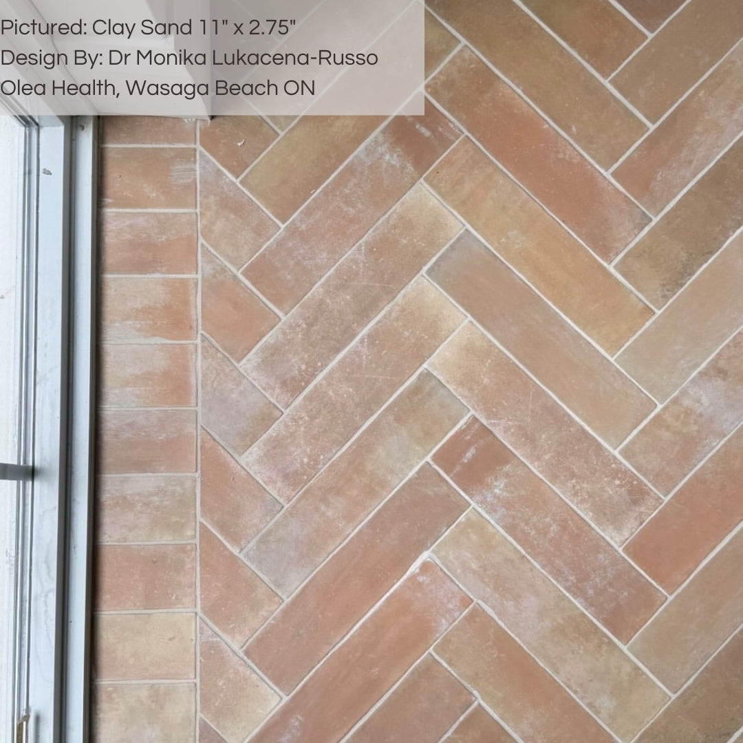 A commercial floor installation of 11x2.75 brick clay sand beige stone look tile in a herringbone layout, the tiles have heavy colour variation, a matte finish, and a natural looking edge