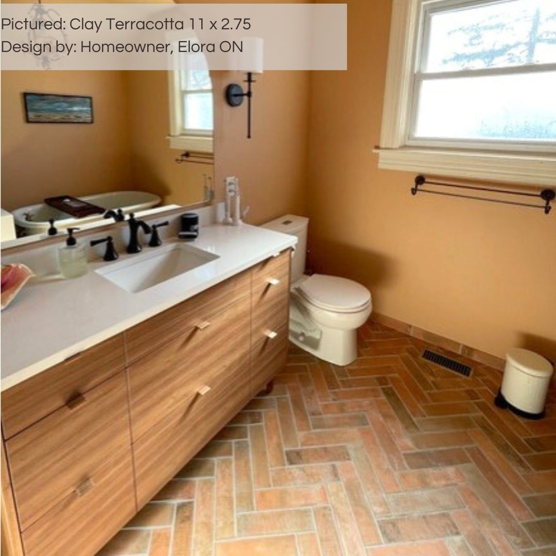 A warm natural vibes bathroom with Tuscan gold walls, light wood furnishings and clay terracotta brick look 11x2.75 tiles on the floor in a herringbone layout. 
