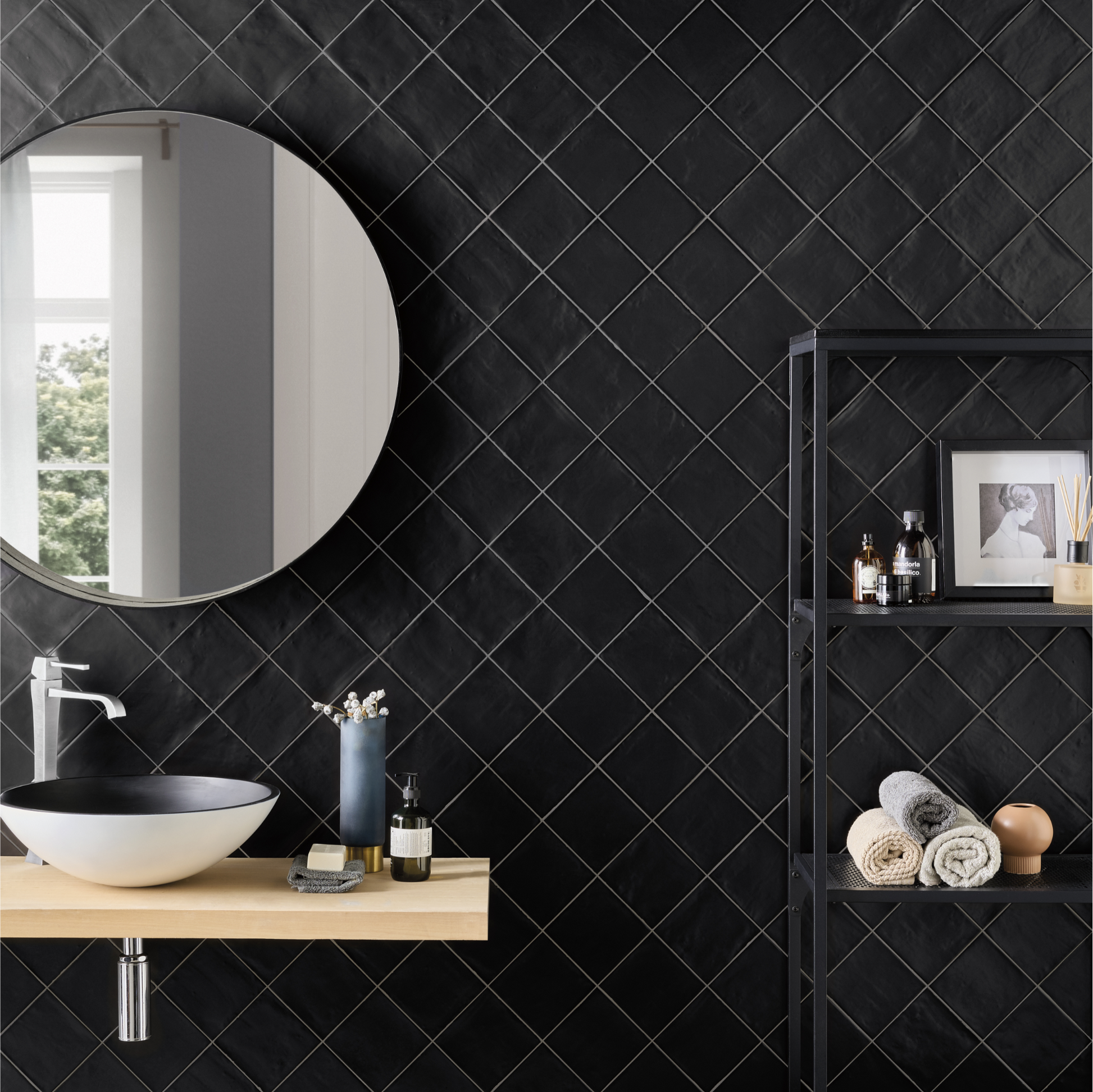 A modern black and white powder room. There's a bathroom vanity with a matte black tiled backsplash. The tiles are installed in a diamond pattern along the entire wall, the surface of the tiles are uneven and the edges of tile are tumbled catching the light. 