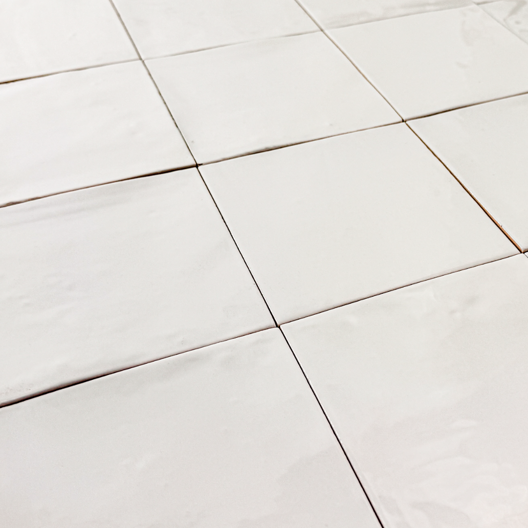 Angled close up view of a group of glossy 5x5 textured  powder white tiles showing the textured edges. 