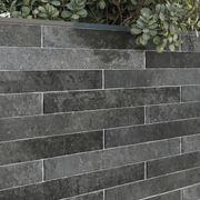 A close up view of an exterior application of tiles on a planter box. The greenery pops against the charcoal black 2x18 brick look tiles that are installed in a traditional horizontal brick pattern. There is colour variation and textured look in the tiles. 