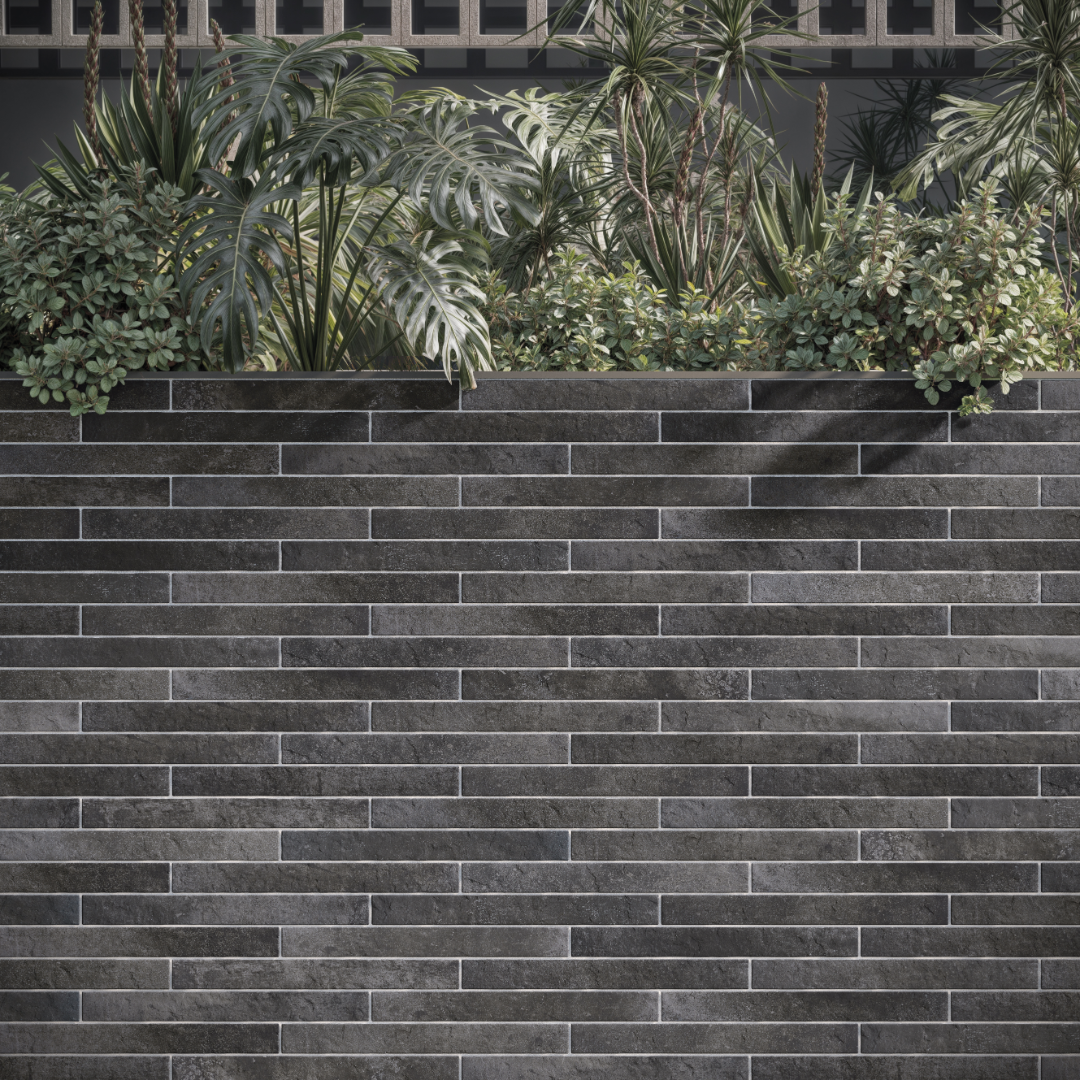 An exterior application of tiles on a planter box. The greenery pops against the charcoal black 2x18 brick look tiles that are installed in a traditional horizontal brick pattern.