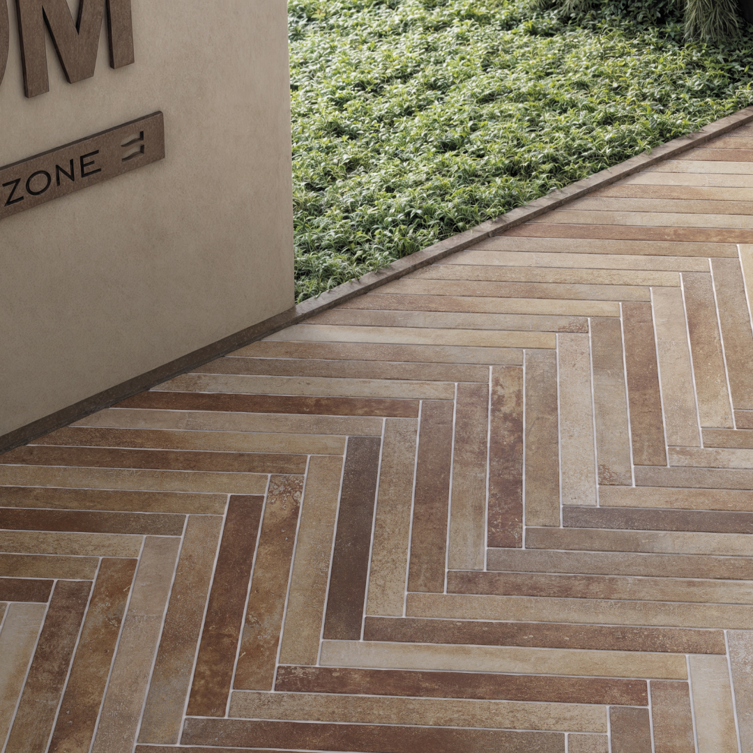 Angled ariel view of terracotta brown 2x18 brick look tiles installed in interior and exterior herringbone floor brick pattern. Showing colour variance, texture and the finish. 