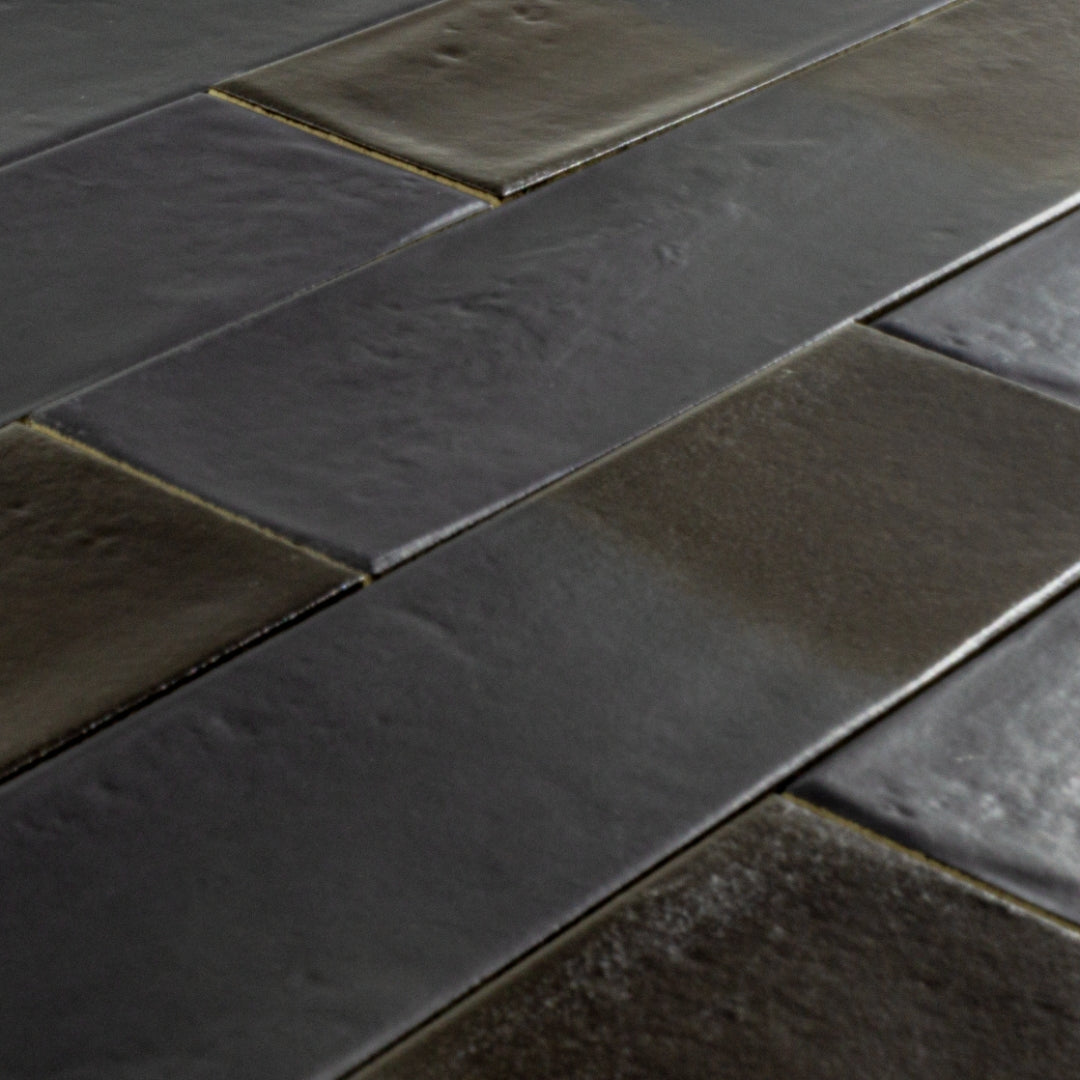 Angled close up of 3x12 glossy textured black tiles in a brick layout showing the finish and colour variance. 