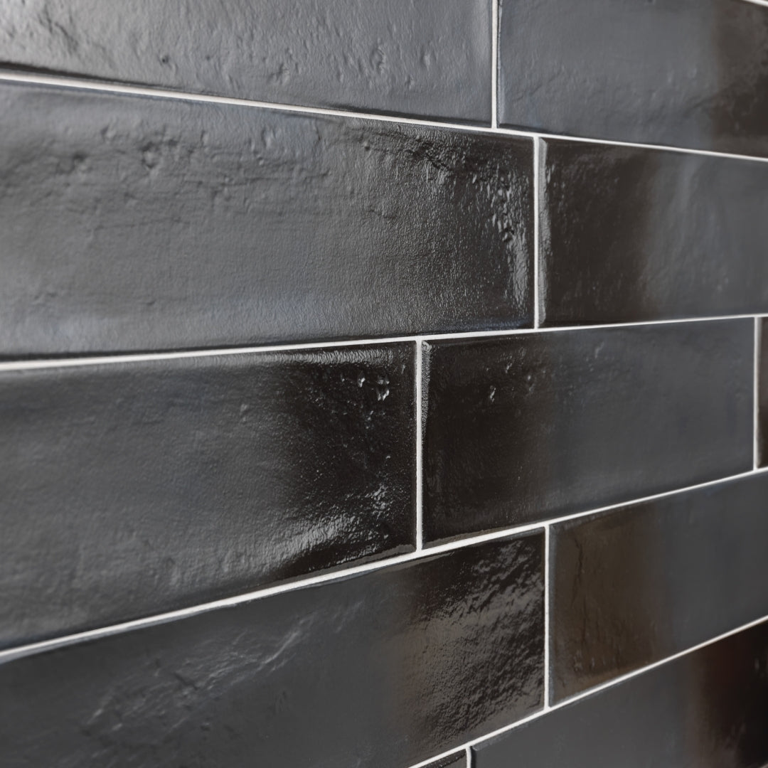 Angled close up of 3x12 glossy textured black tiles in a brick layout showing the light grout, tiles finish and colour variance. 