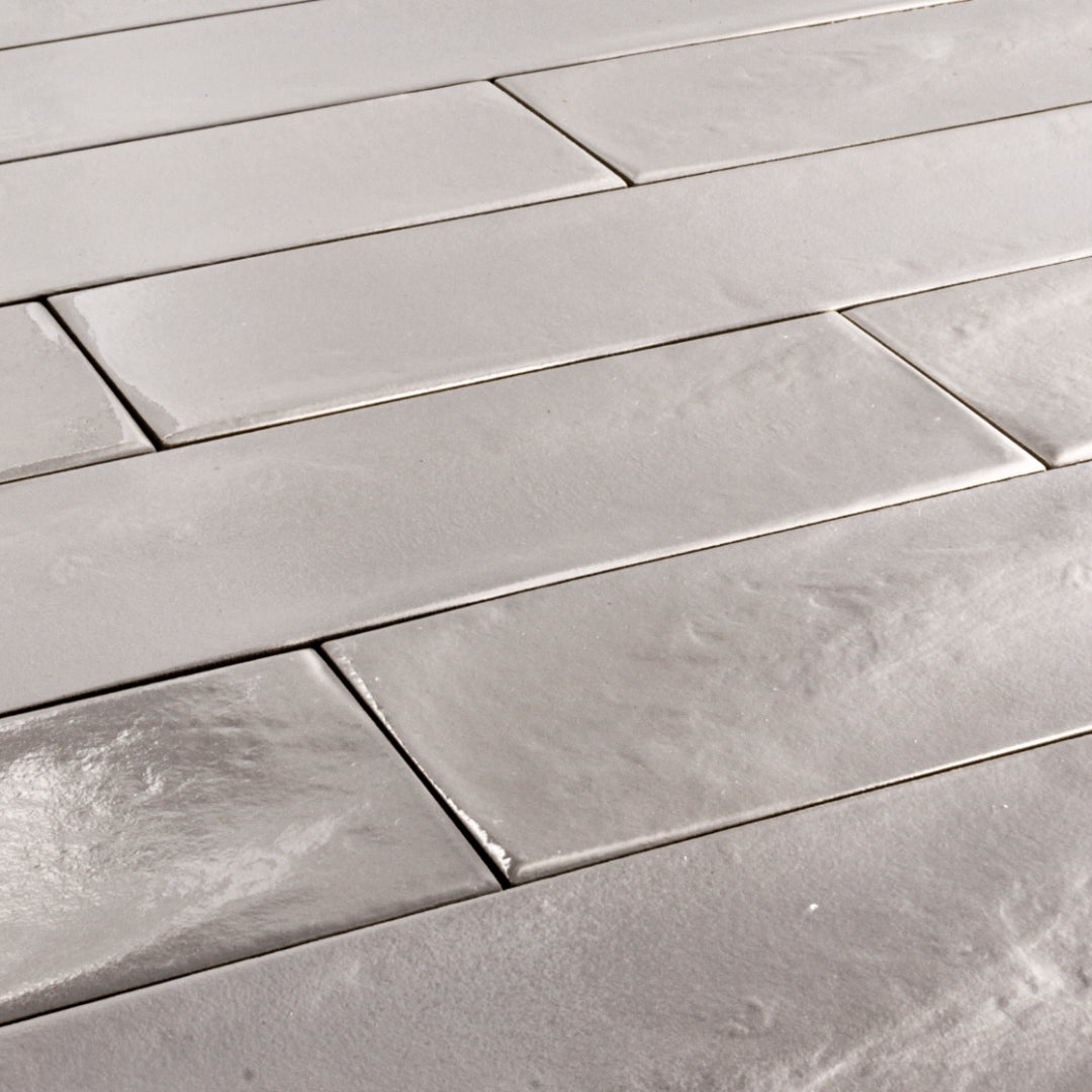 Angled close up of 3x12 glossy textured light grey tiles in a brick layout. 
