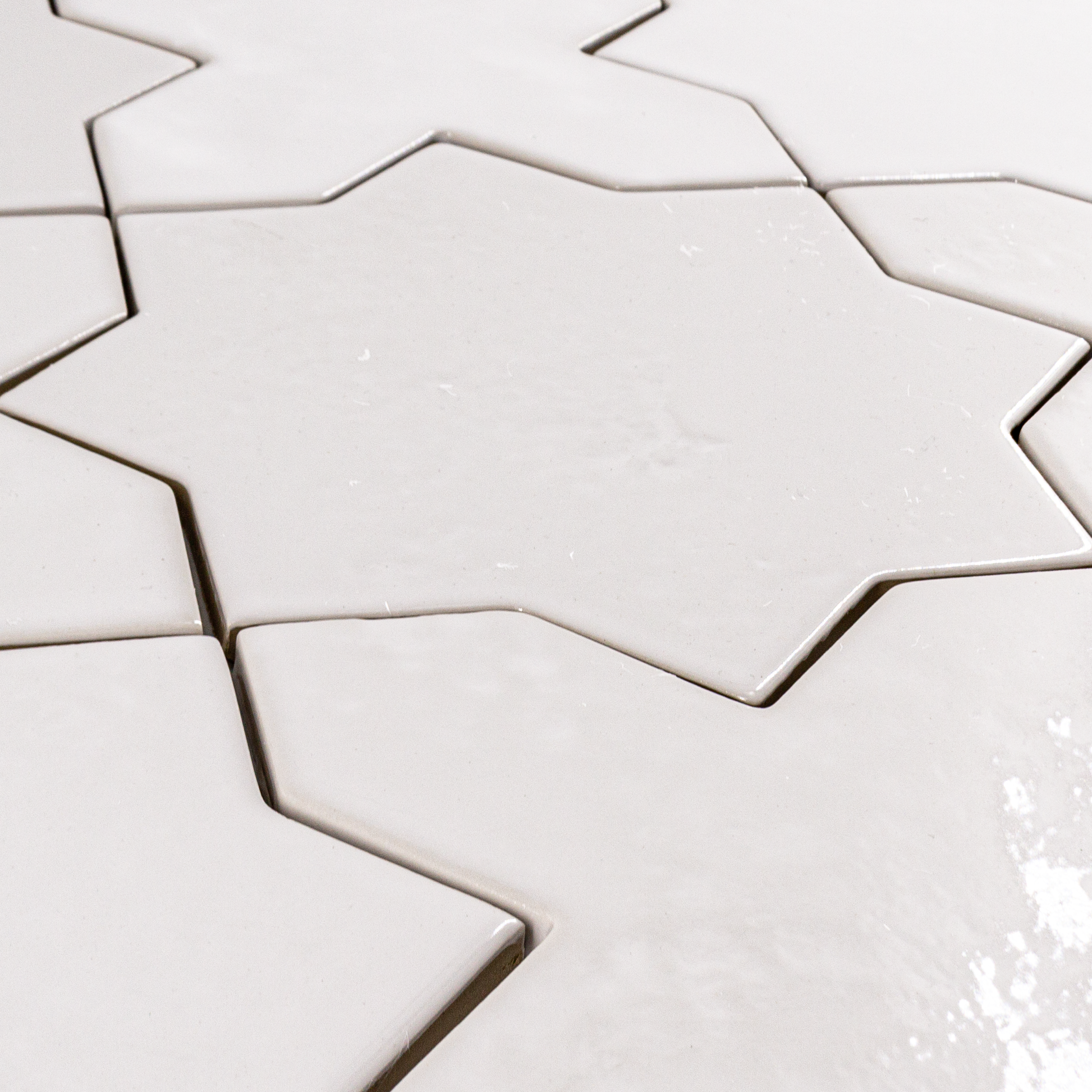 Angled close up of a group of star and cross shaped tiles interlocking together in a glossy white finish.