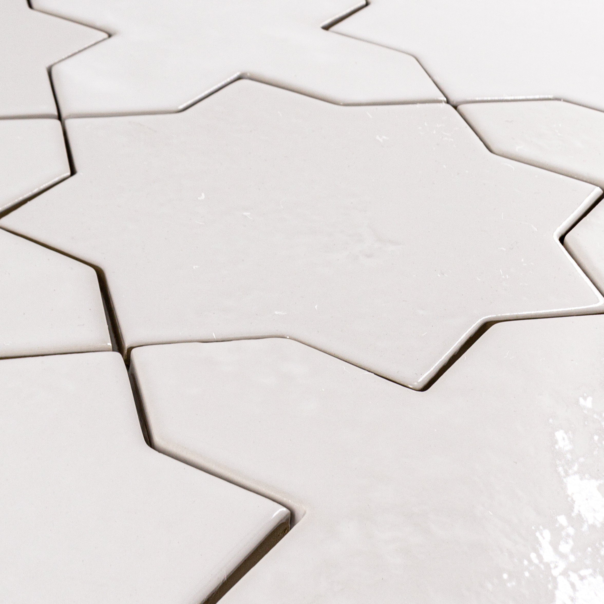 Angled close up of a group of star and cross shaped tiles interlocking together in a glossy white finish.