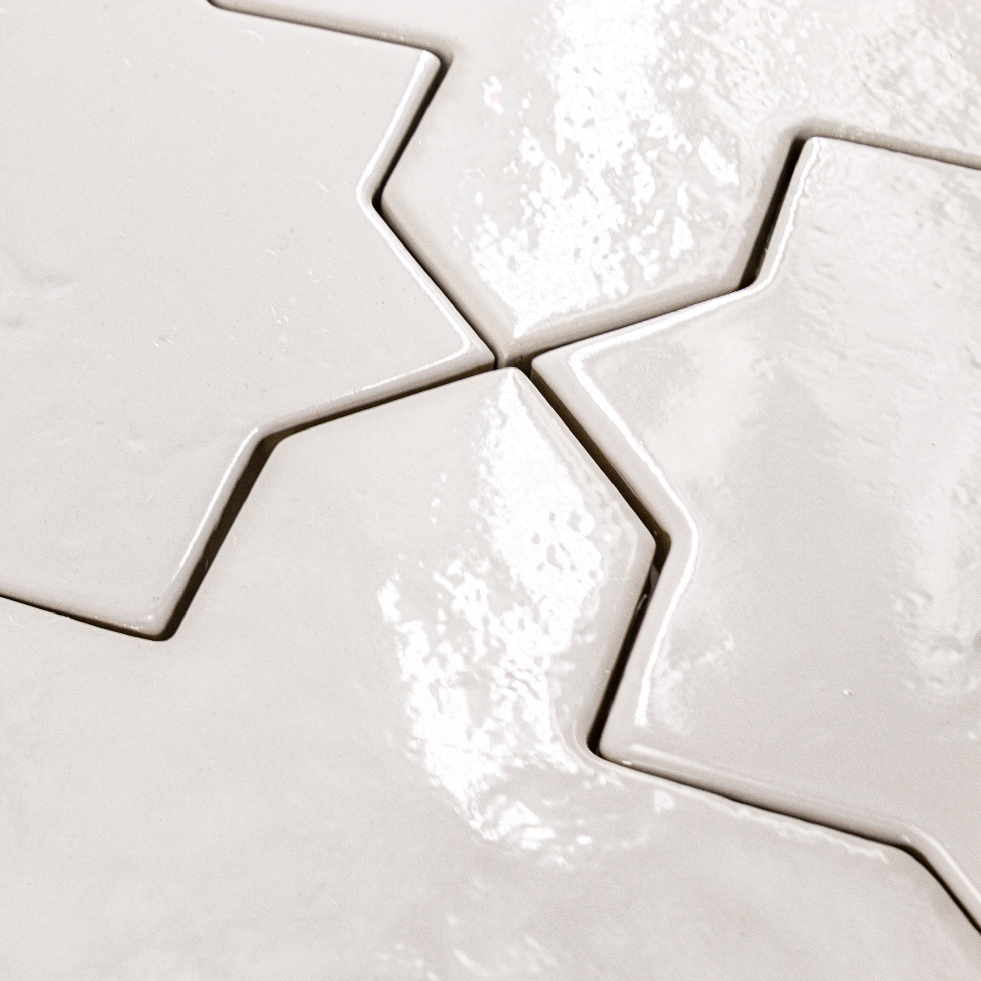 Angled close up of a group of star and cross shaped tiles interlocking together in a glossy white finish.