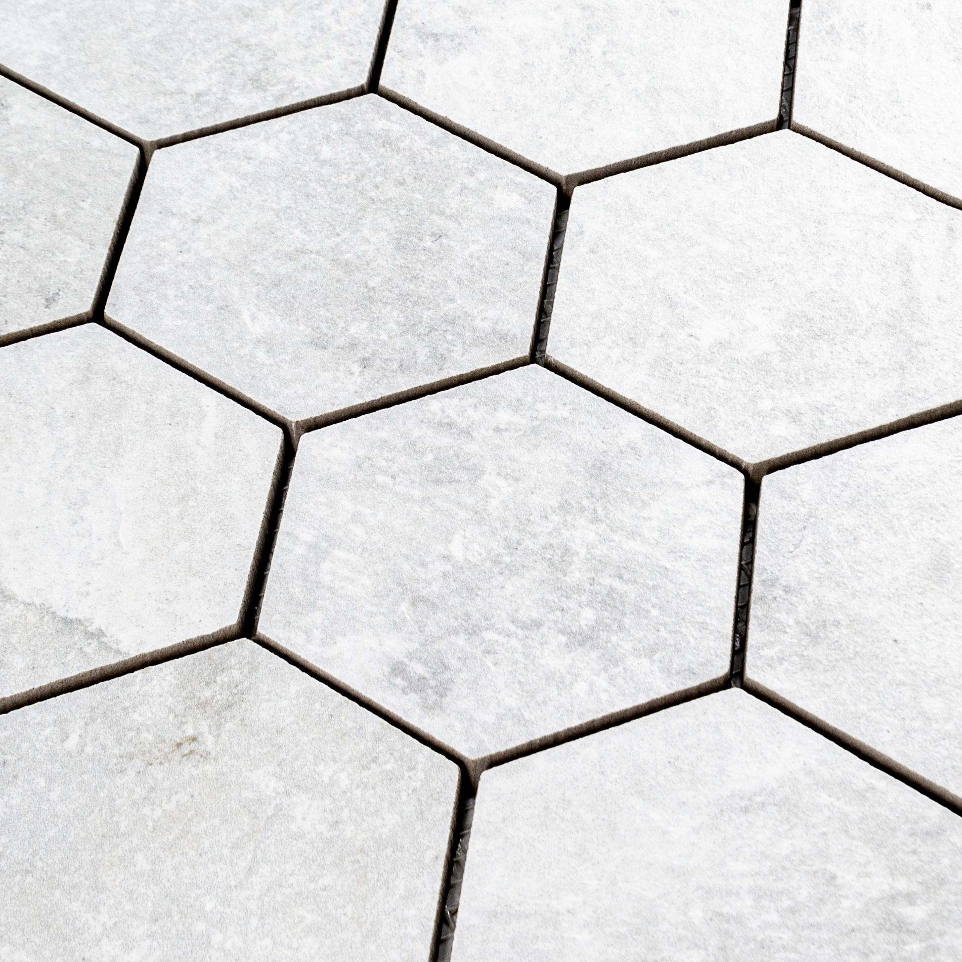 Angled ariel view of A 3" hexagon mosaic tile in a light white stone look showing the colour variation and texture. 