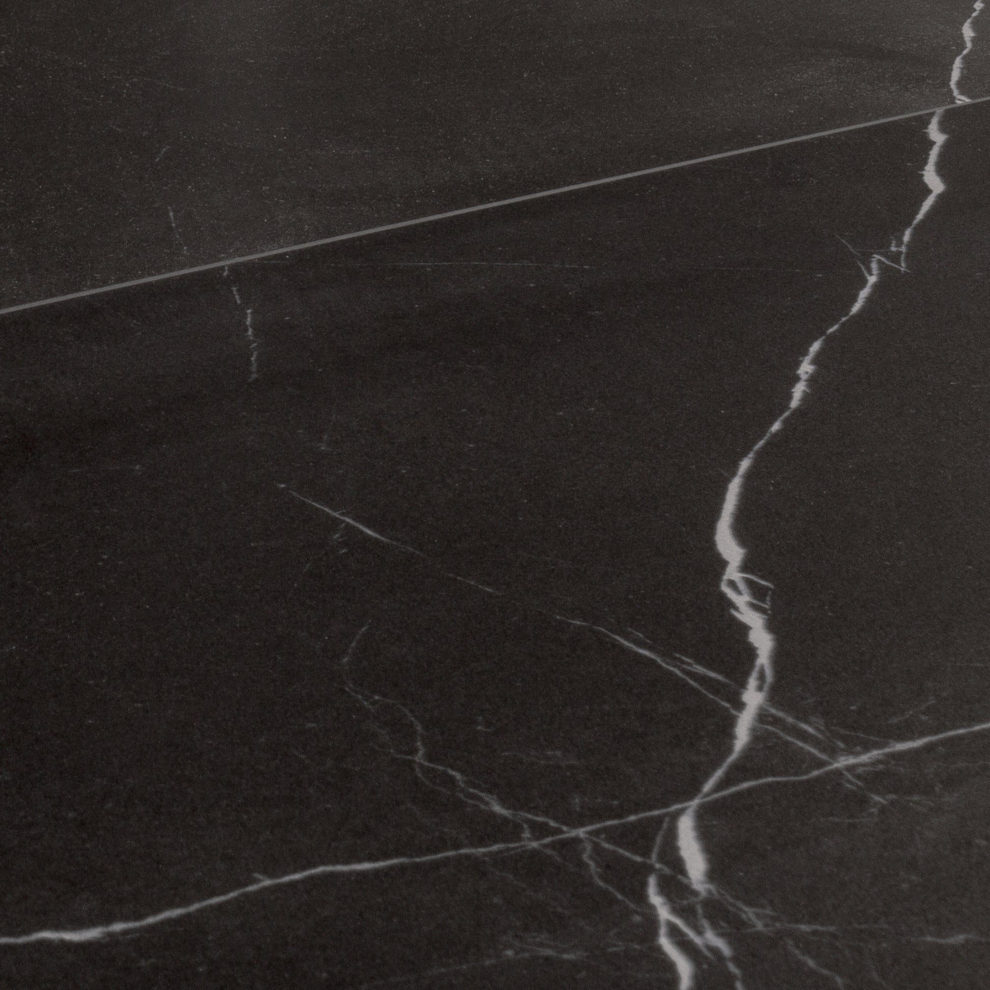 Angled close up view of 24x48 tiles in matte black marble look porcelain with white veining. 