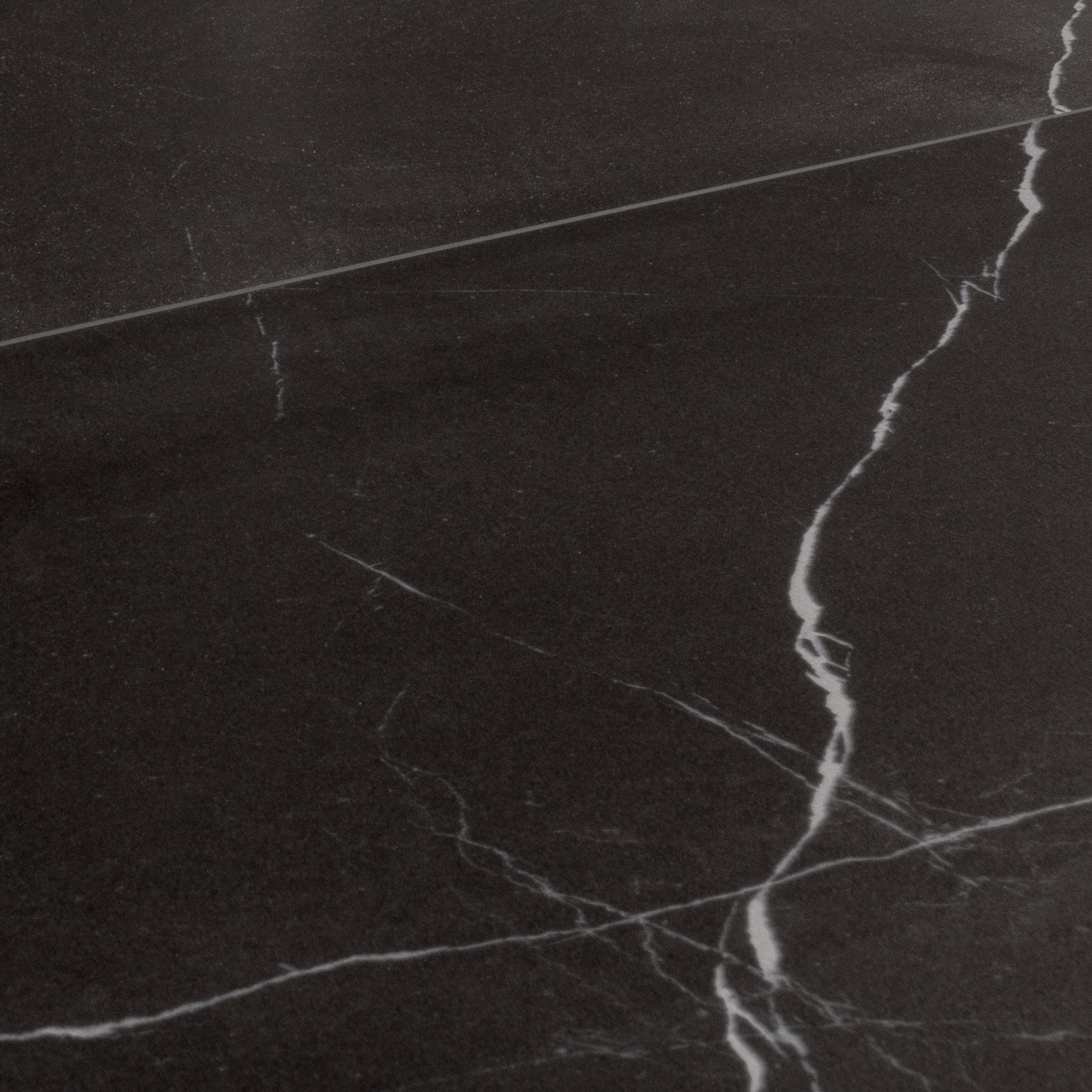 Angled close up view of 24x48 tiles in matte black marble look porcelain with white veining. 